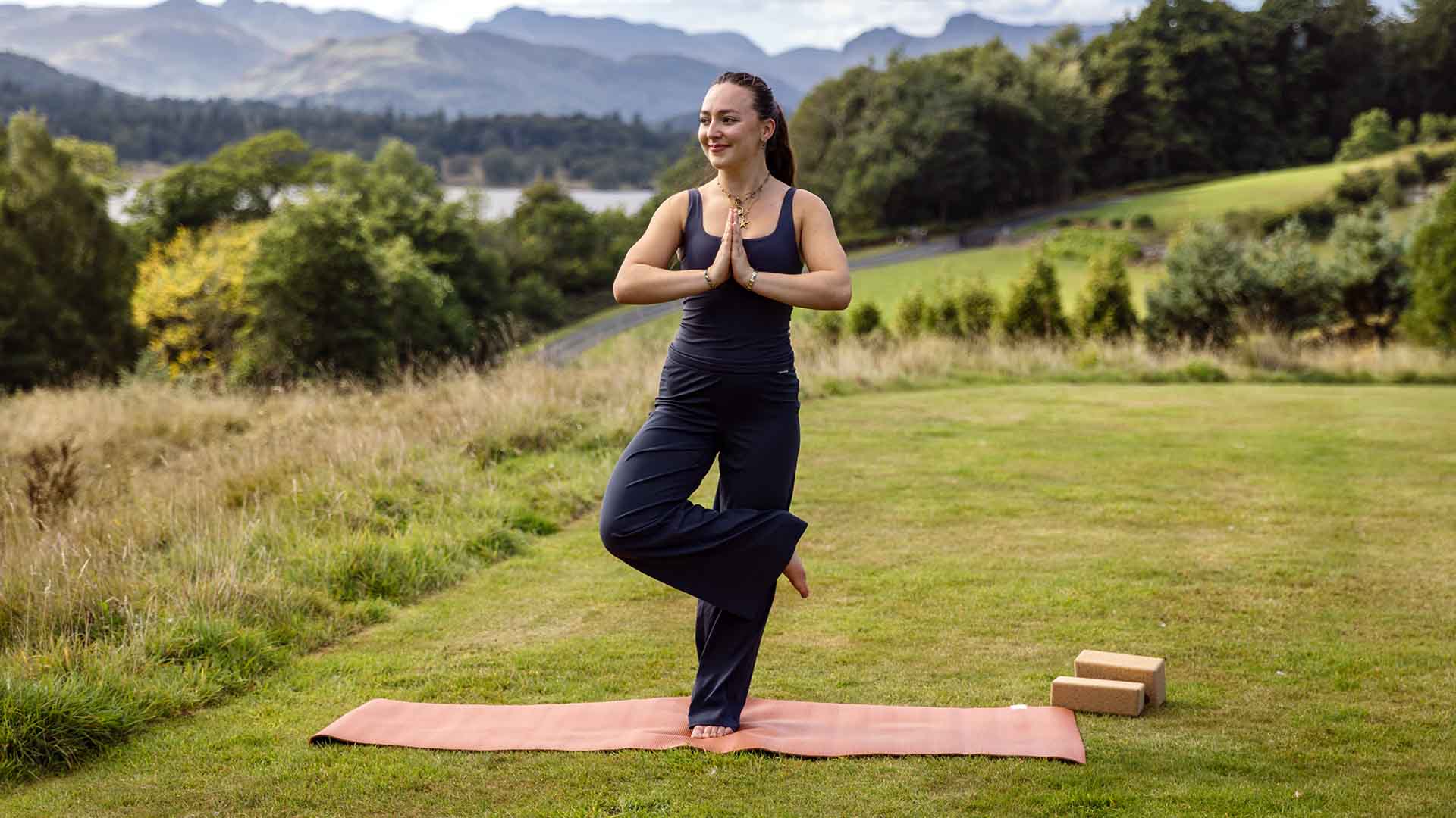 Milly  stood in a yoga pose on the fell above Low Wood Bay