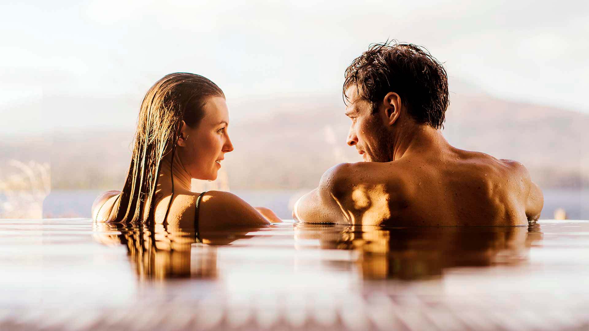 Couple looking at one another with views over Windermere behind in the indoor Spa