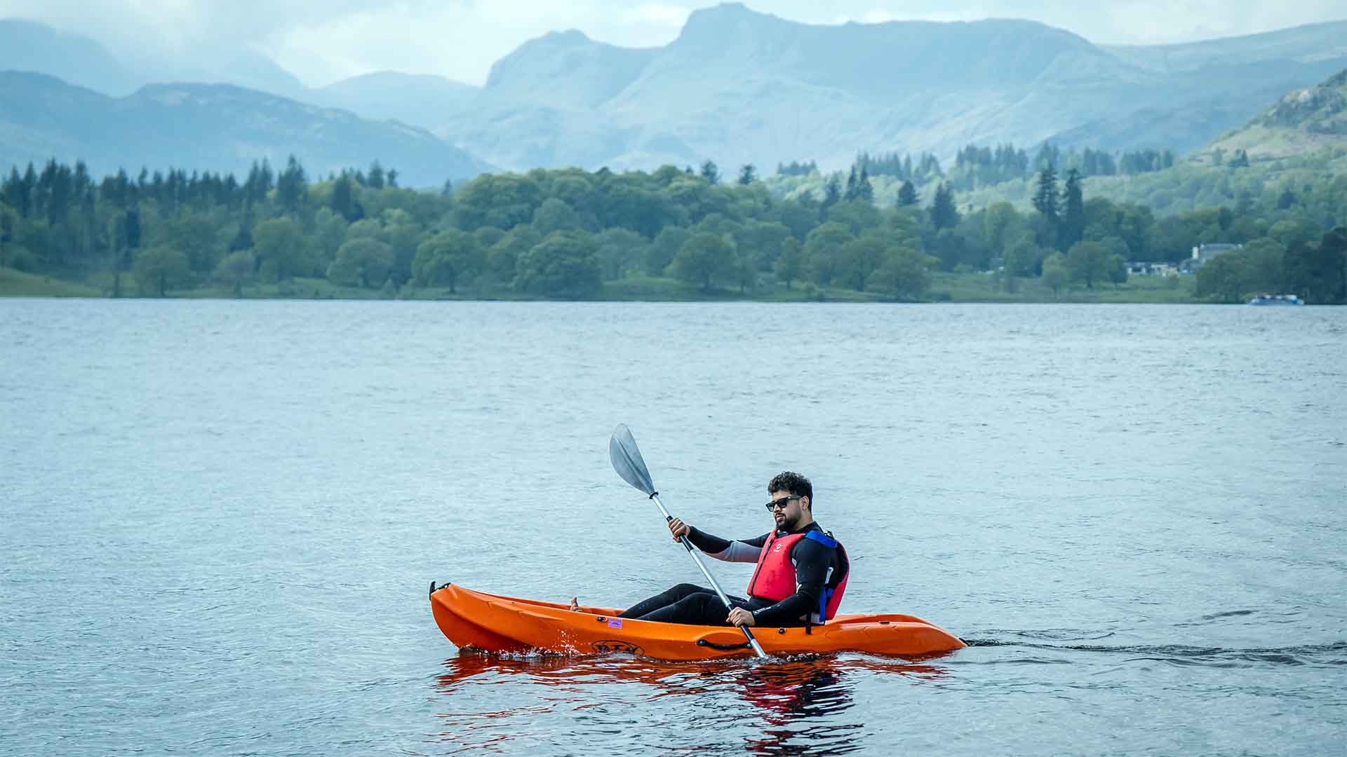 Man on a single sit-on kayak on lake Windermere with the Lake District fells in the background