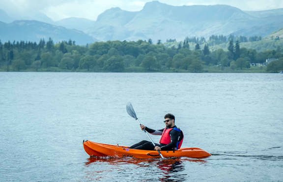 Young man paddling a hired, sit-on-top kayak on lake Windermere