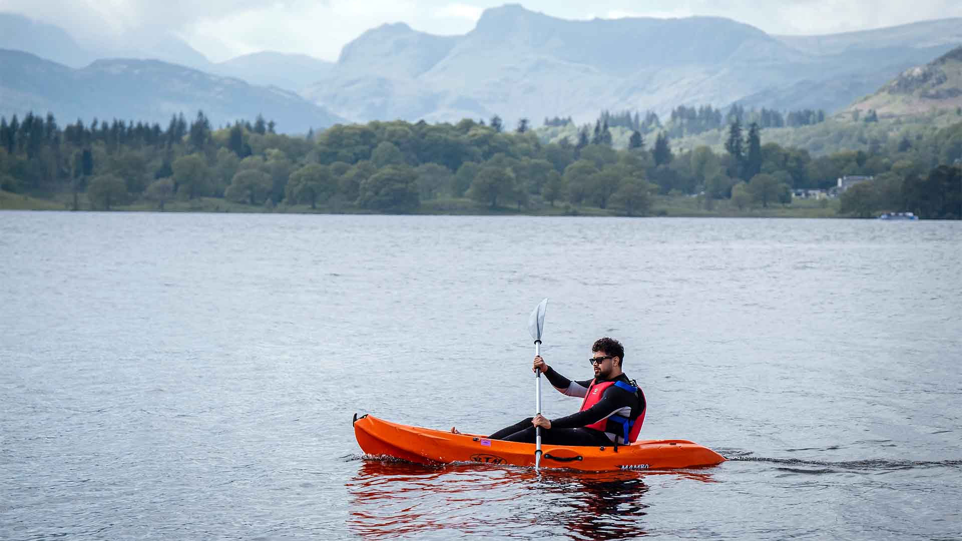 Man on a single sit-on kayak on lake Windermere with the Lake District fells in the background