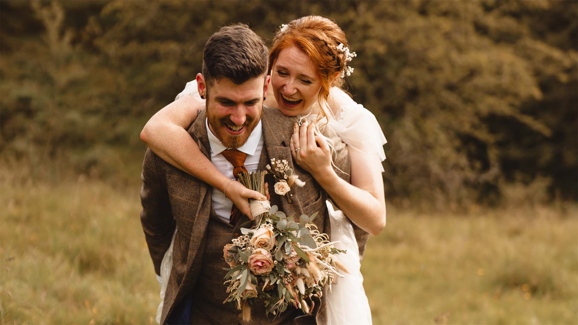 Bride being given a piggy back by the groom on a path in the Wild Boar Estate woods