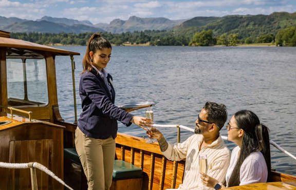 Young woman serving Champagne to two guests aboard the Winander launch.