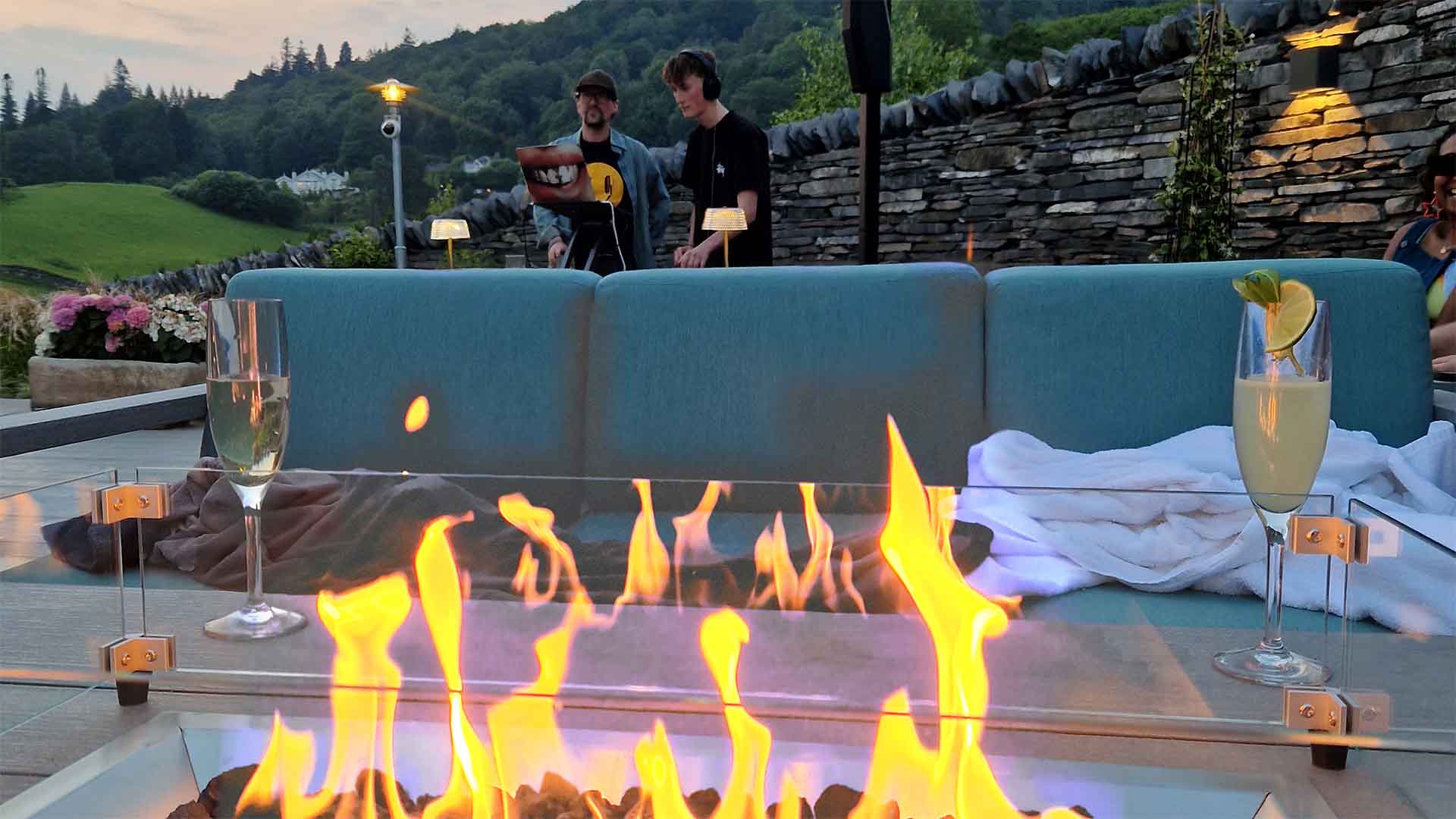 A firepit with seating and the DJ desk behind by the pool