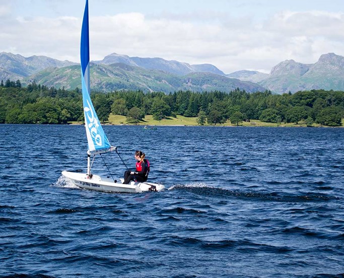 Young woman sailing a Pico solo with Langdale pikes behind