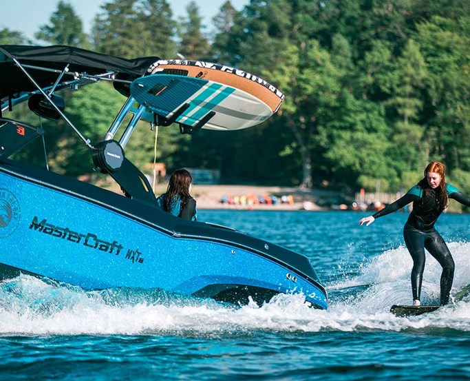 Young woman wakesurfing behind mastercraft boat