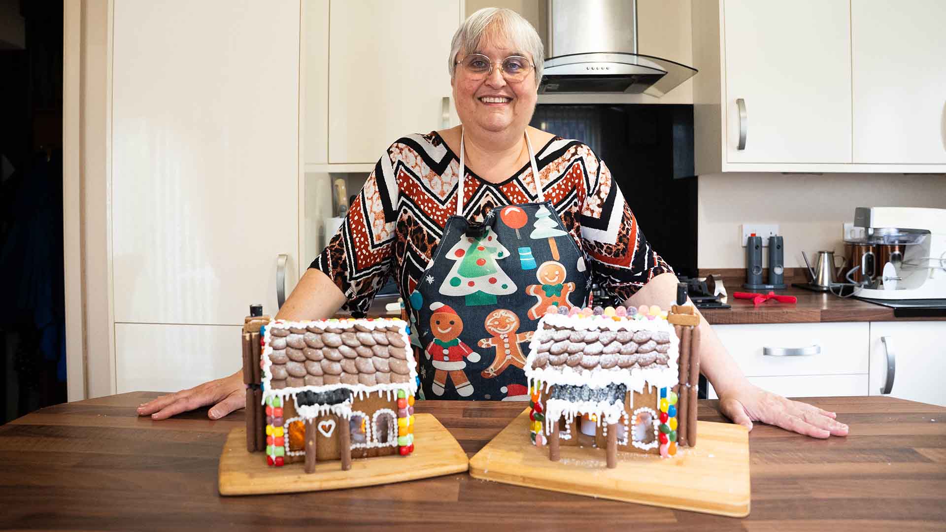 Baker in her kitchen with 2 gingerbread houses
