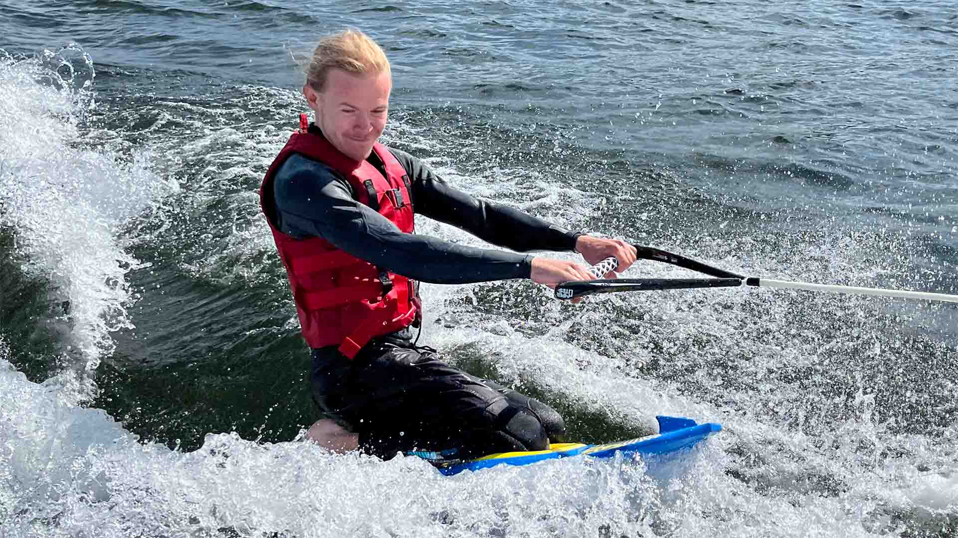 Young man kneeboarding on lake Windermere, aside the boat