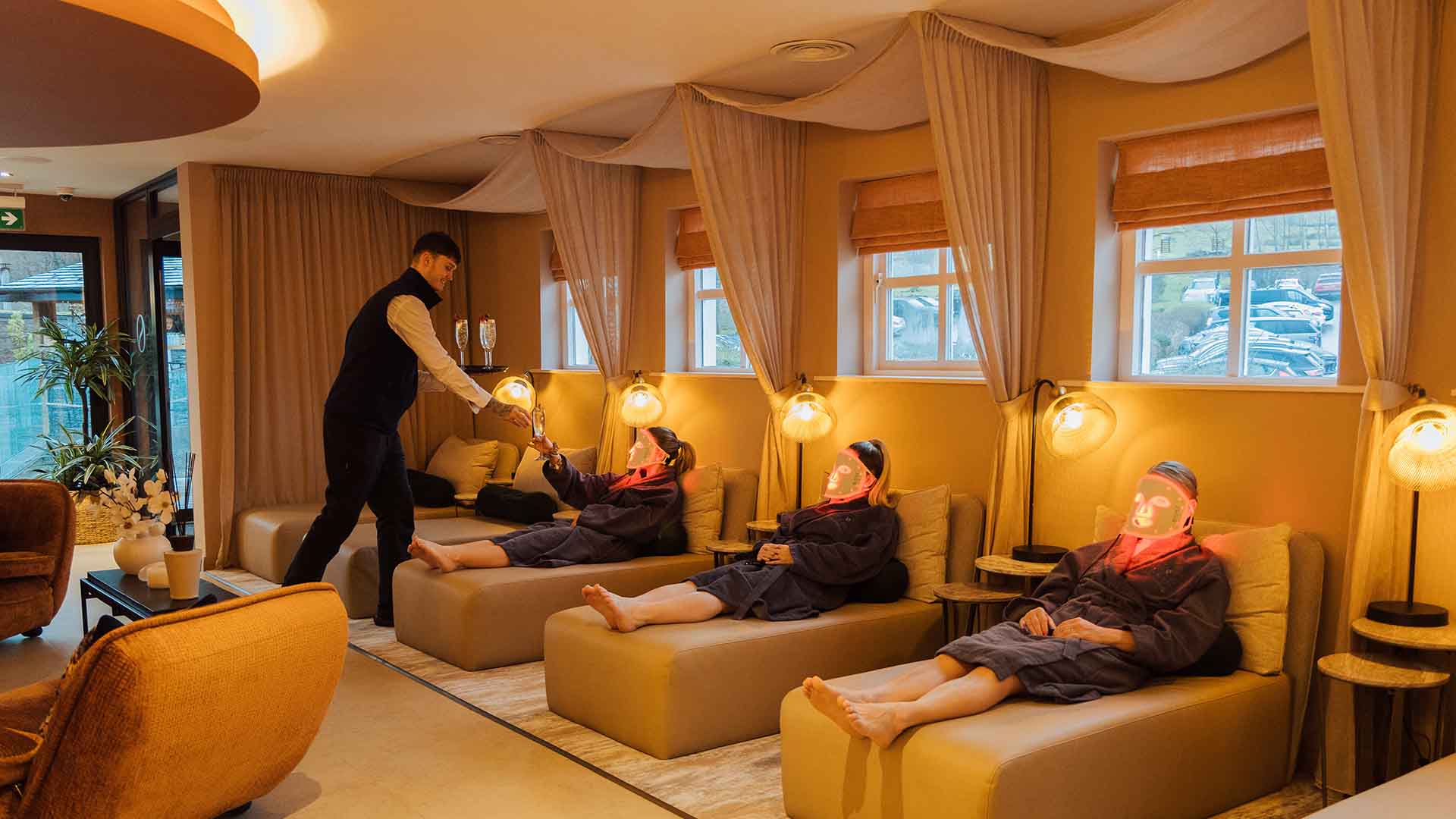 Three young women laid on loungers been served a drink whilst enjoying the LED experience in the spa lounge