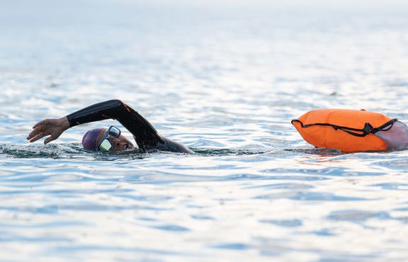Swimmer in open water wearing wetsuit and using orange float