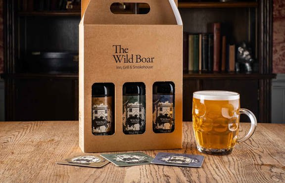 Pack of Wild Boar Estate beers on a table with a glass of beer.