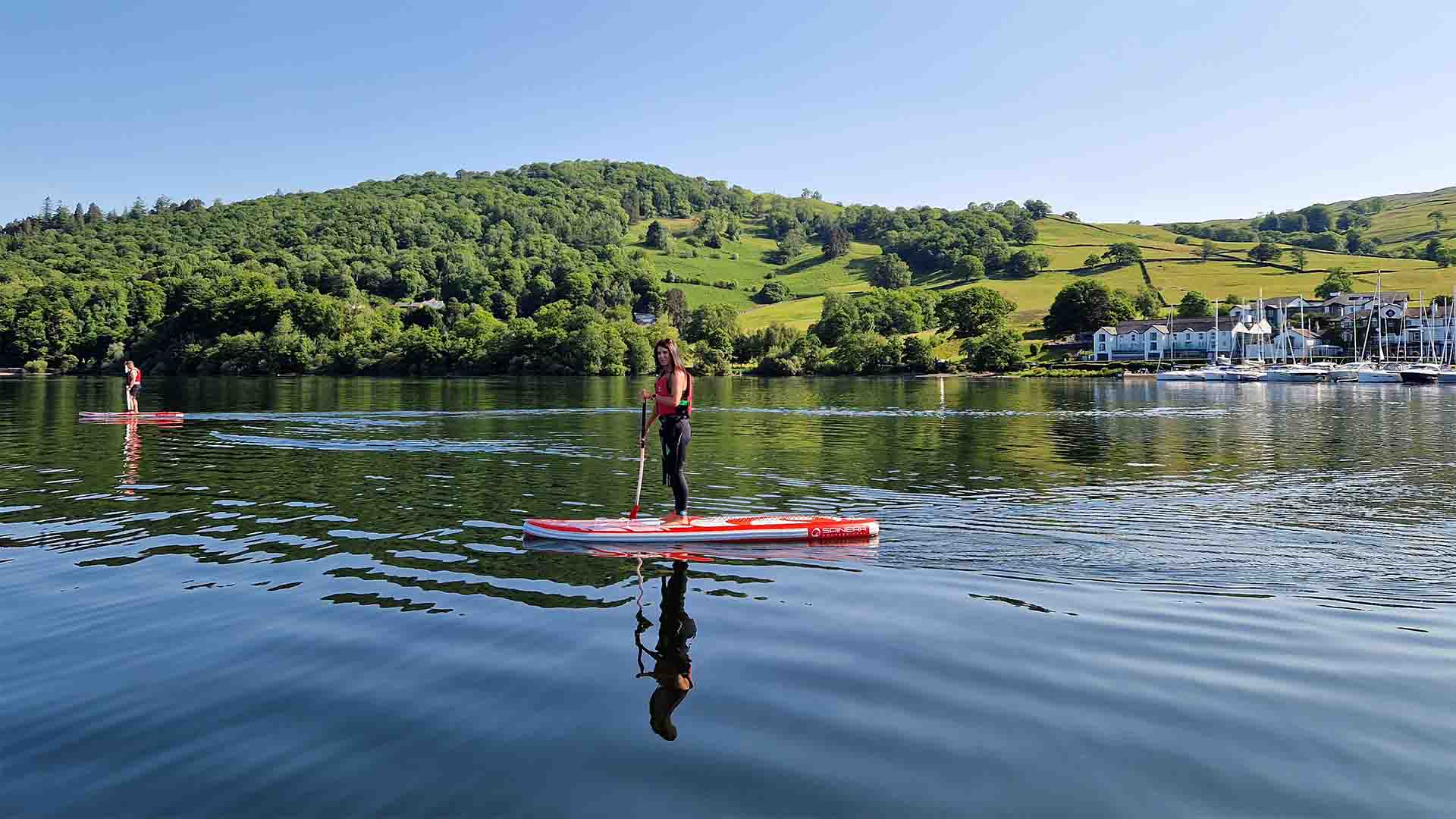 Young woman on a paddleboard on lake Windermere in front of Low Wood Bay