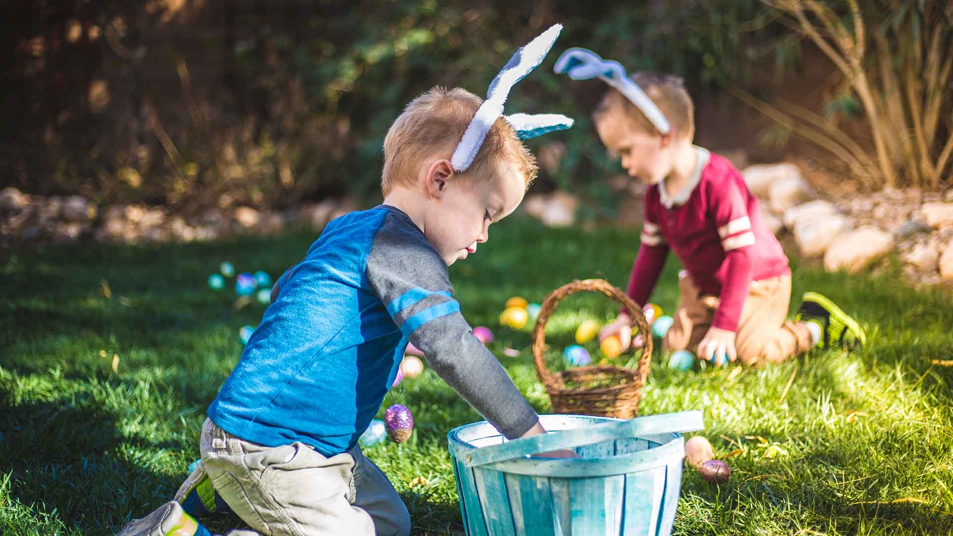 Two young boys collecting easter eggs in a garden.