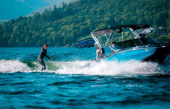 Young woman wakesurfing on lake Windermere behind a mastercraft boat