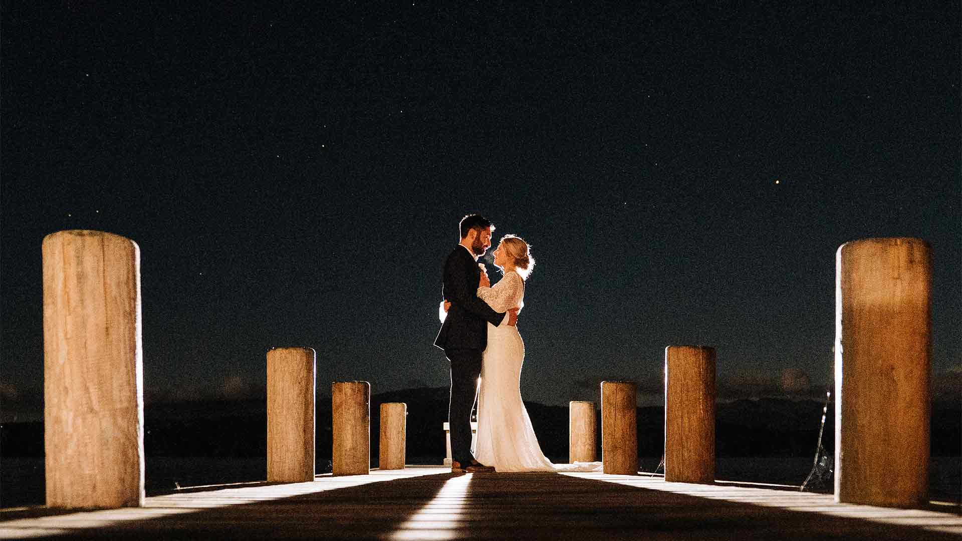 Couple on the jetty at night with a light throwing them into silhouette