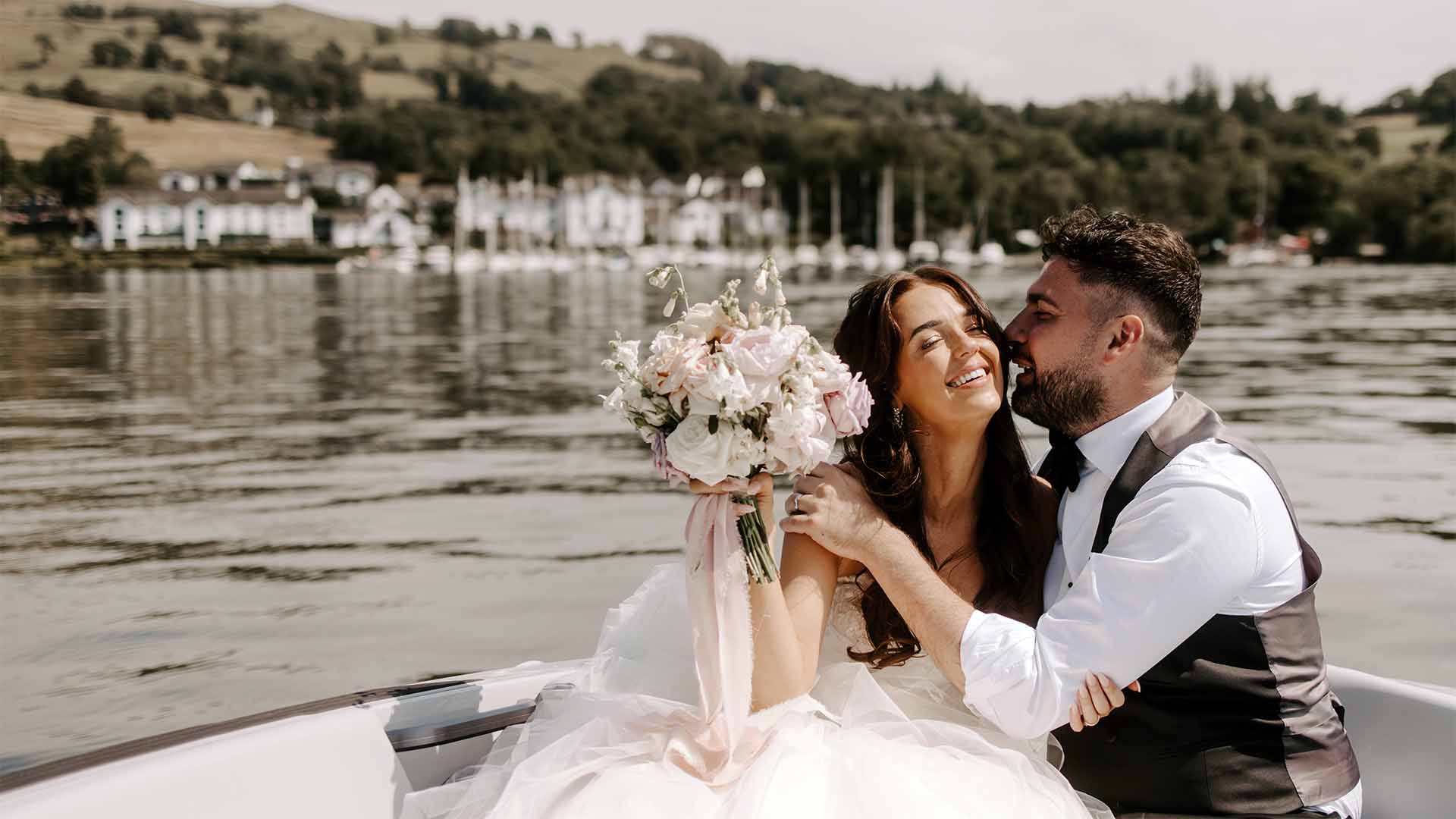 newly wed couple in a boat on Windermere with Low Wood Bay behind