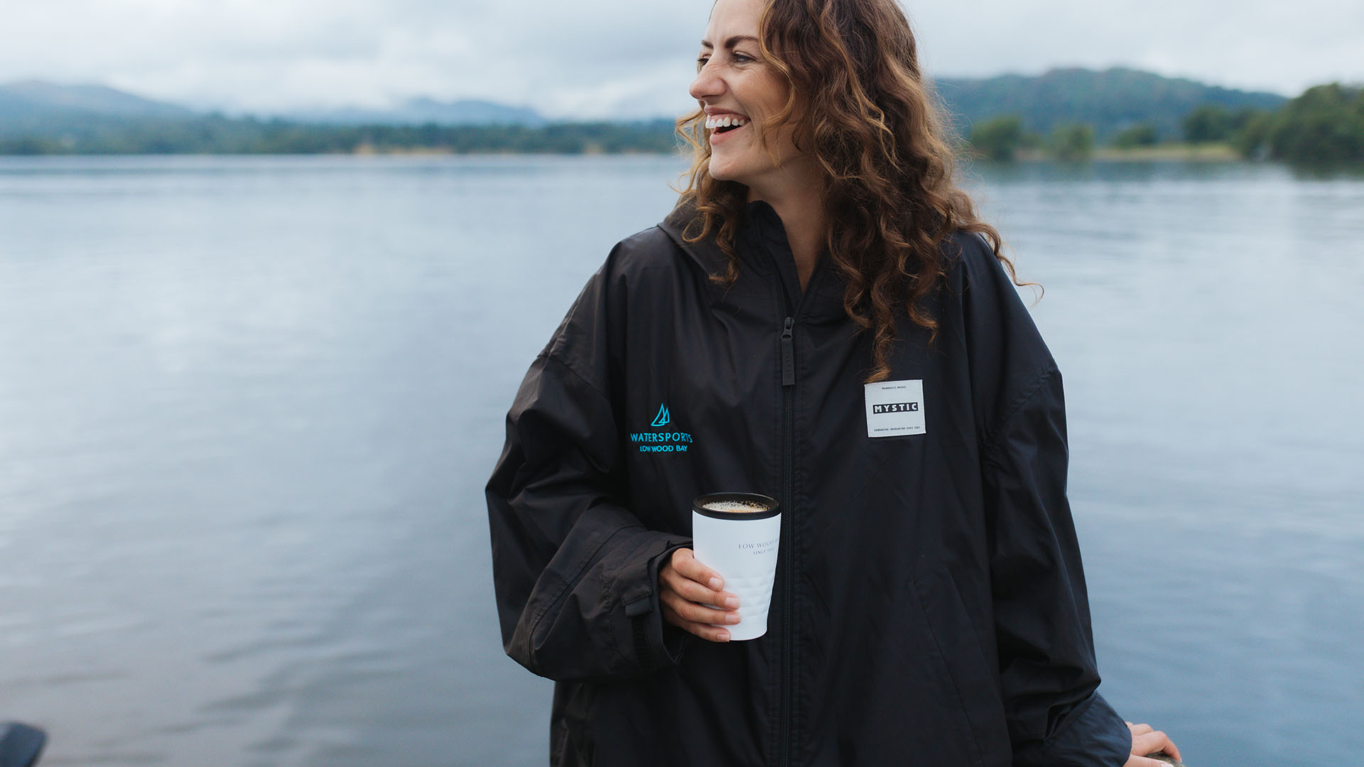 Young woman stood by the lakeshore, cup in hand.