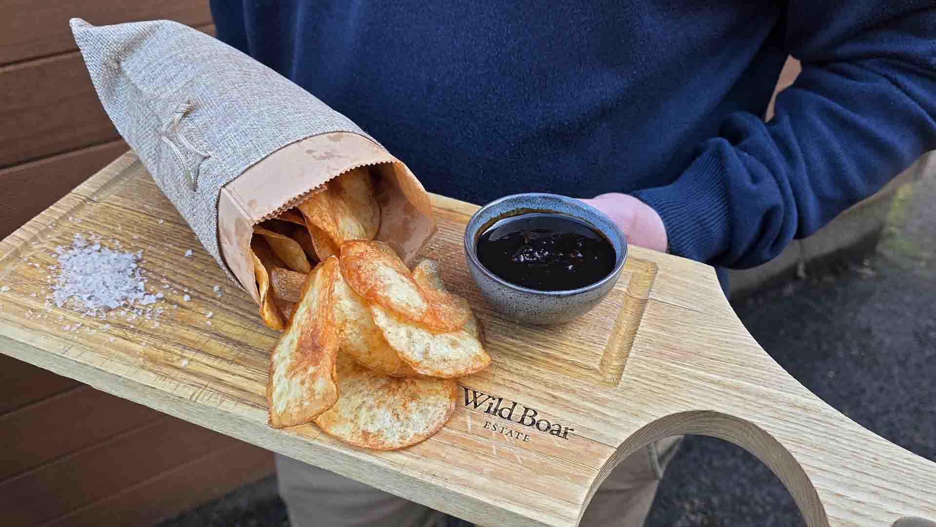 Home-made crisps on a wooden board with a dip and salt