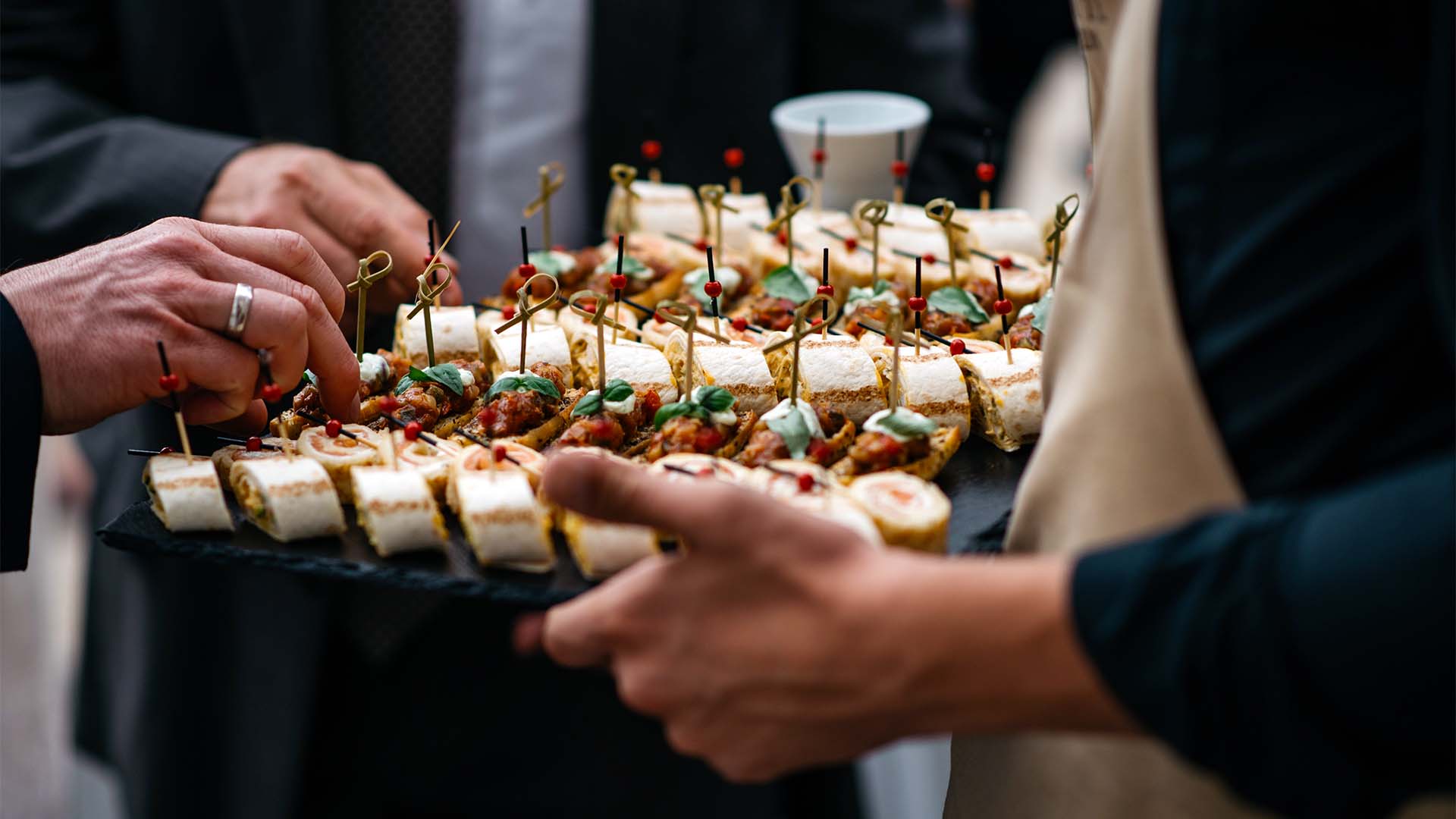 Waiter holding a tray of finger food with 2 people selecting items