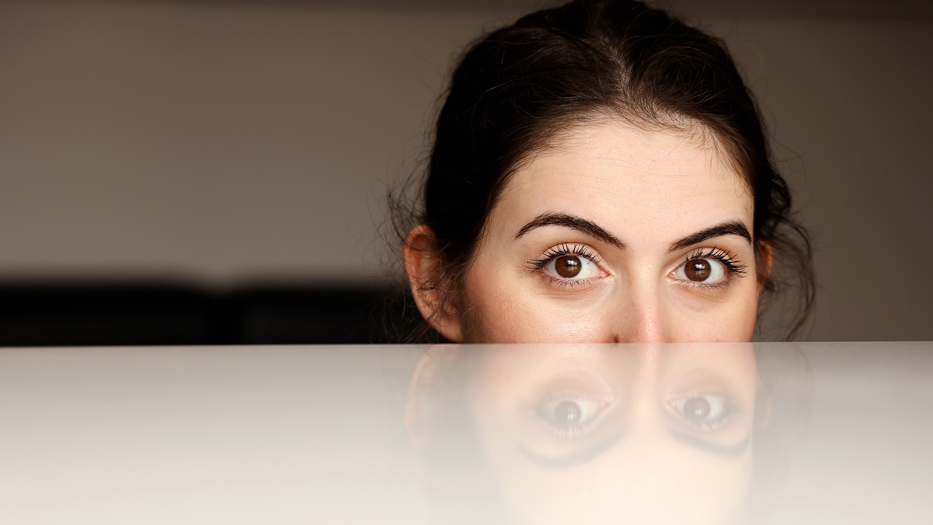 Young woman part hiding face below a desk
