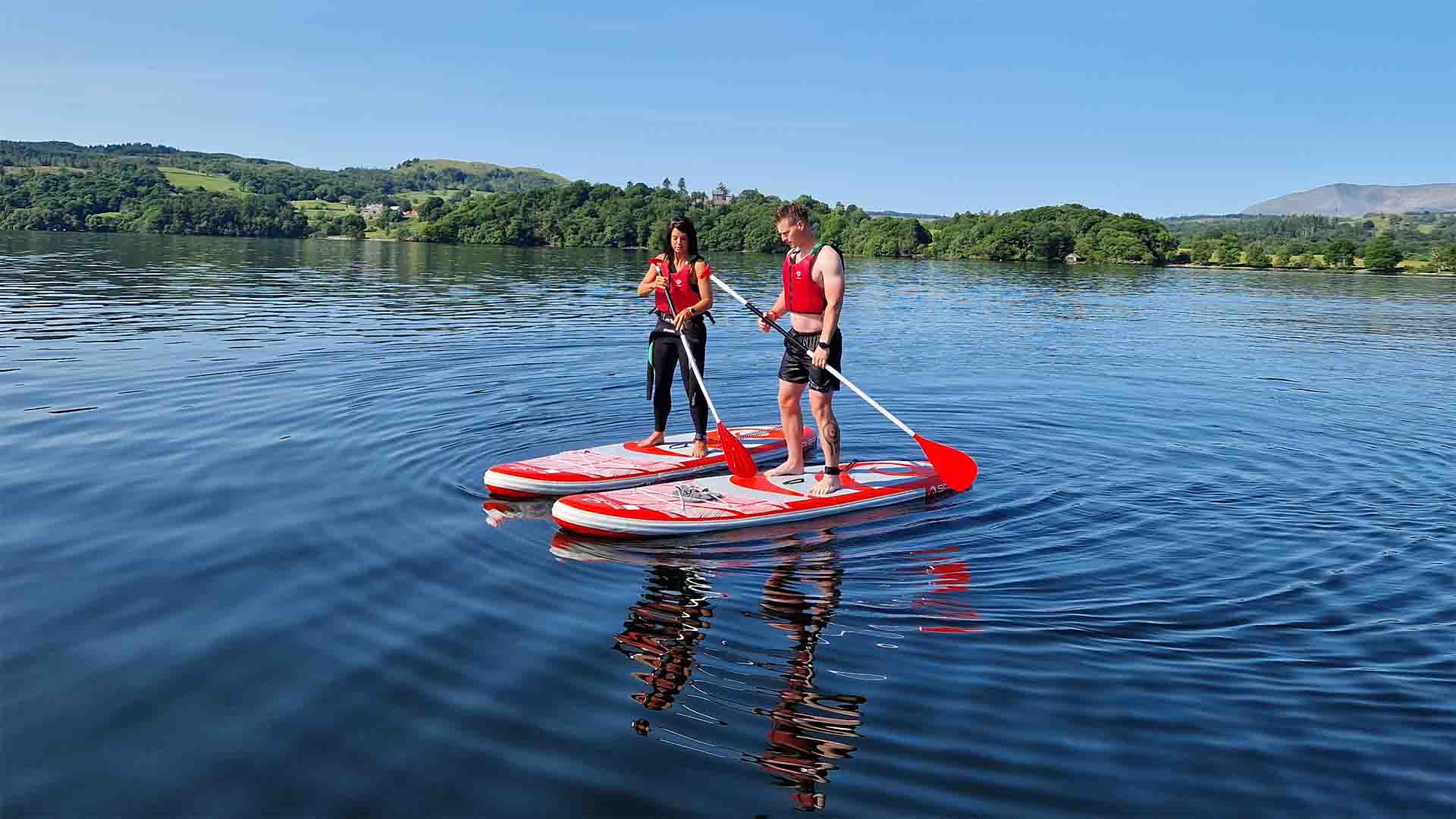 Couple paddleboarding on lake Windermere with the Lake District fells in the background