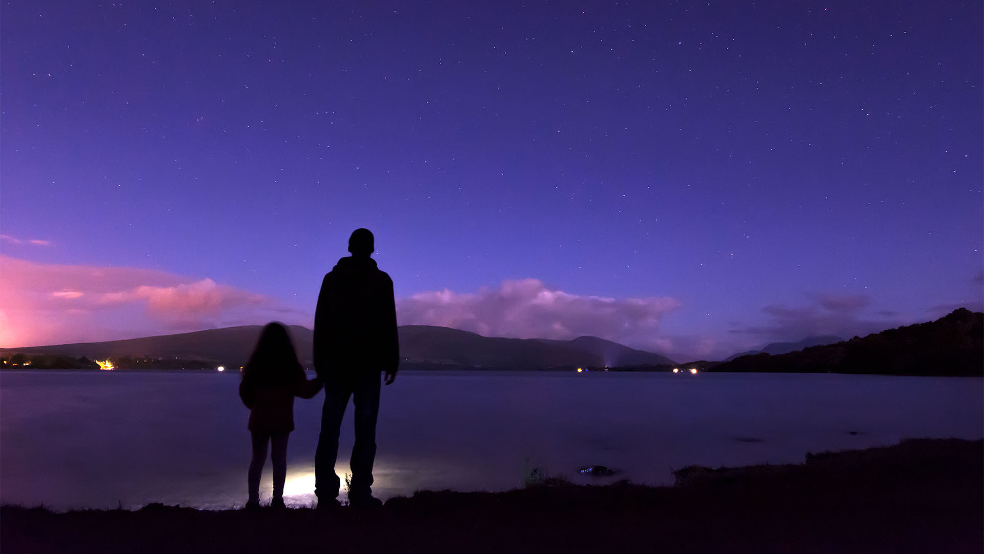 Father and daughter looking at the night sky by a lake