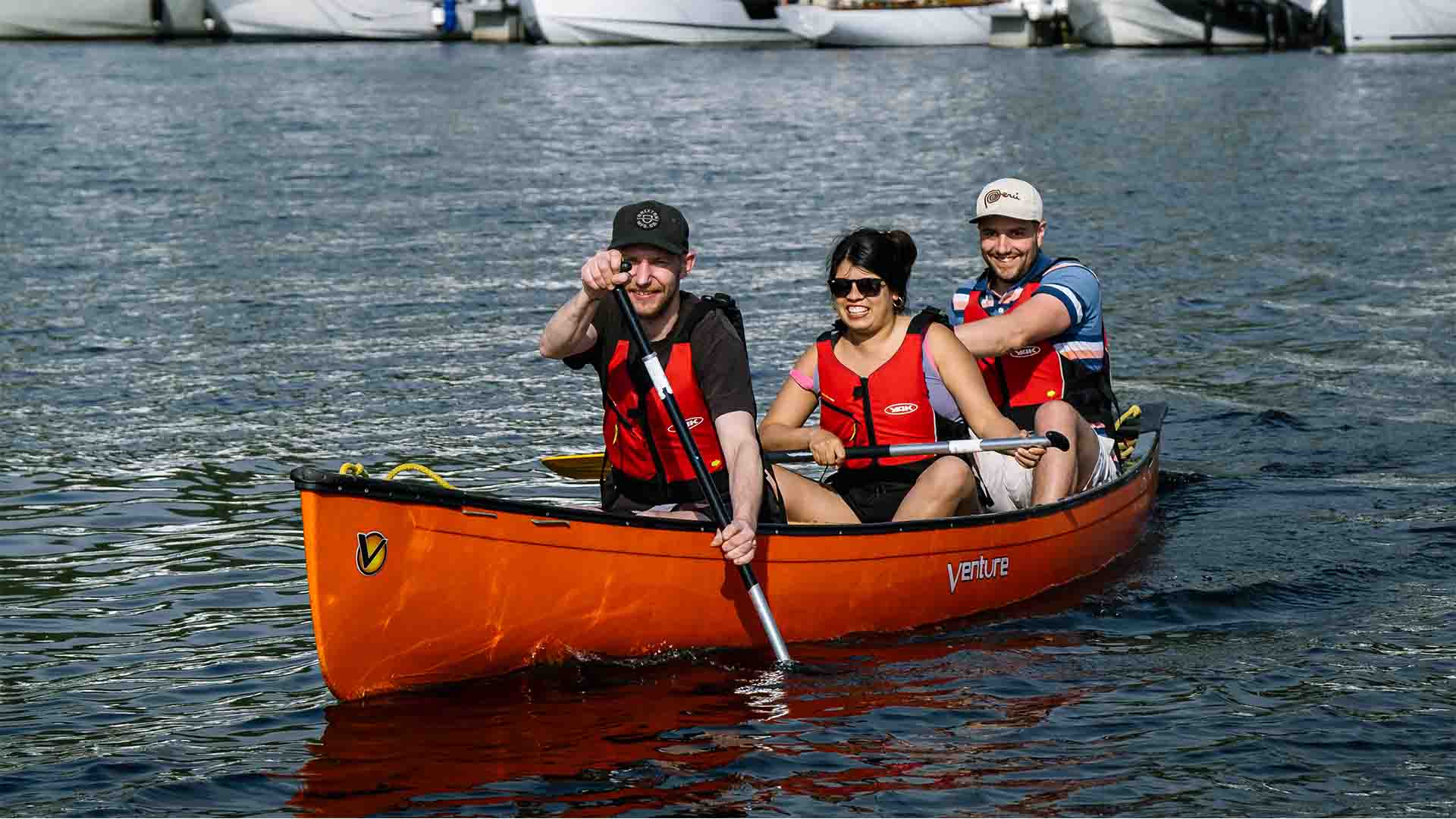 Three people sat aboard a hired open canoe on lake Windermere