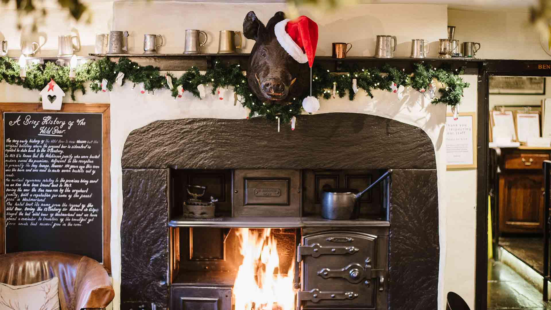 Boars head wearing Santa hat above roaring open fire 