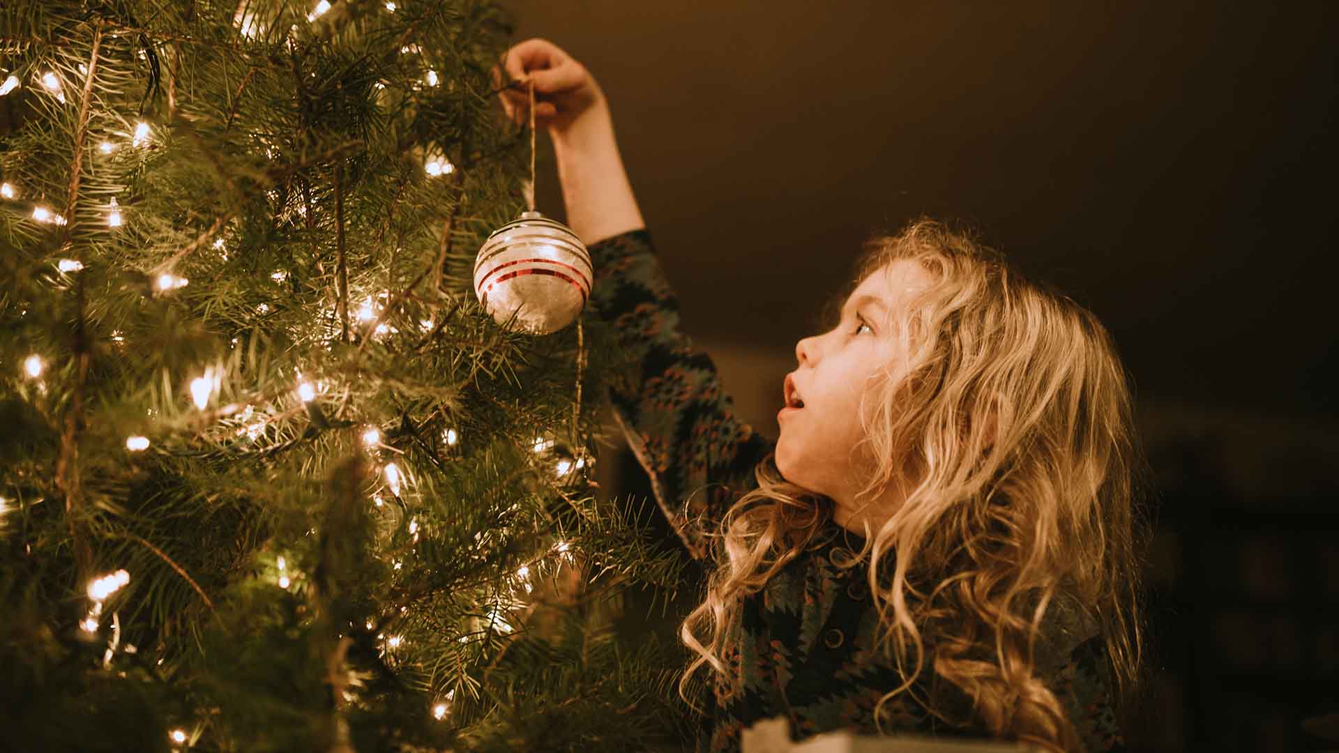 Young girl placing a Christmas bauble on a tree