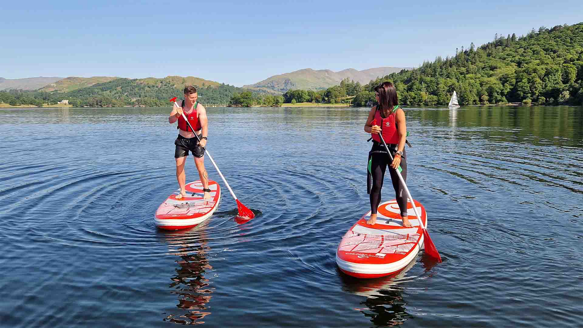 Two paddleboarders on lake Windermere with the Lake District fells in the distance