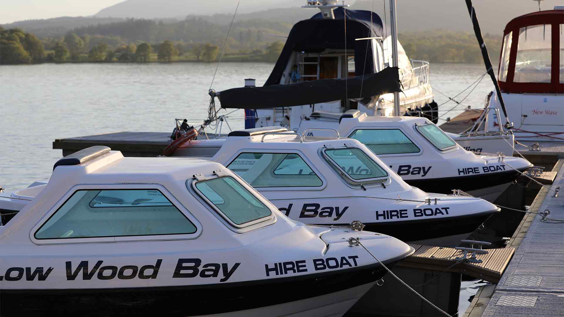 A ine of hire motor boats moored up at the centre's jetty with Windermere behind