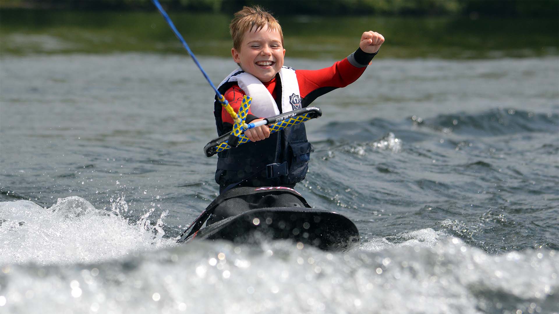 Young boy punching the air, enjoying kneeboarding on lake Windermere