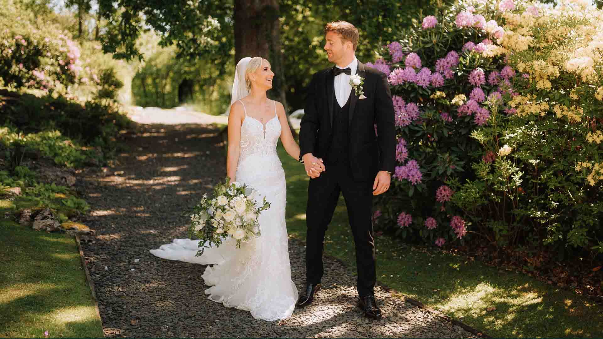 Louise and James walk through dappled light in the hotel gardens